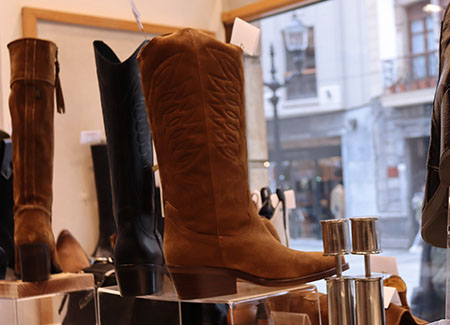 Primer plano de una bota marrón de estilo vaquero, a su lado otra bota del mismo modelo en color negro y, al lado de esta, una bota diferente de color marrón