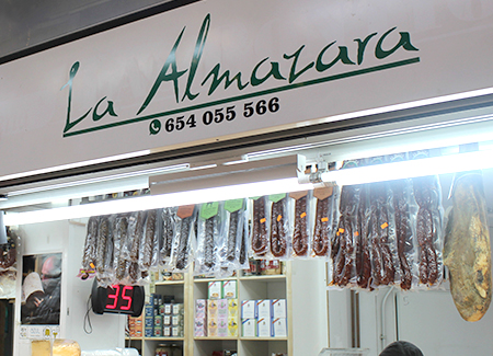 Vista del cartel del comercio. También se pueden ver los embutidos y un jamón colgados del techo