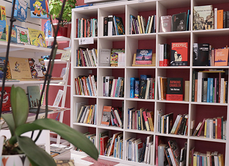 Vista del interior de la librería, dónde podemos ver una estantería grande con libros, al lado de un expositor con más libros destacados. En primer plano vemos unas baldas con libros y cómics en otra pared